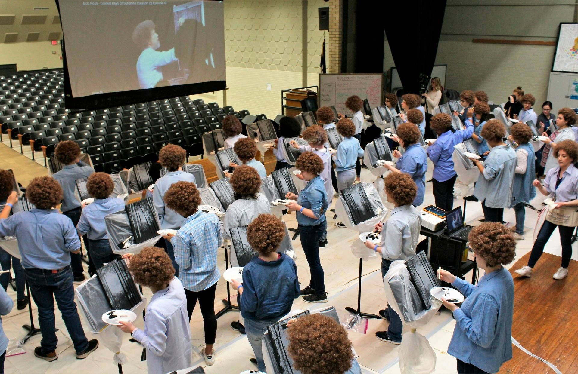Kunststudenten der Madison Middle School in der Nähe von Dallas stehen auf der Bühne des Auditoriums, um unter Anleitung des TV-Kunstlehrers Bob Ross, der auf einer Videowand gezeigt wird, zu malen.