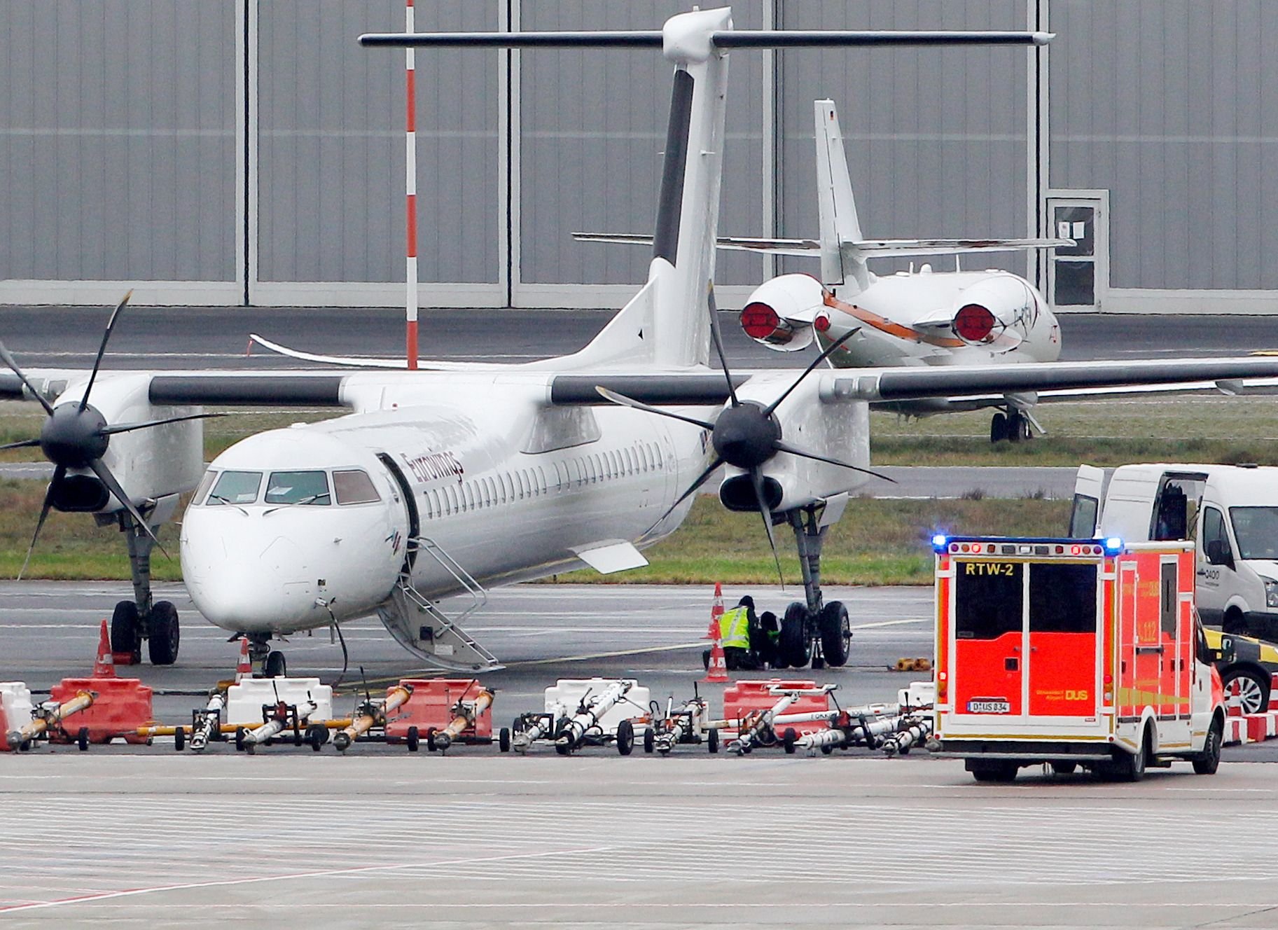 Düsseldorf: Ein Krankenwagen steht neben einem Flugzeug der Fluglinie Eurowings auf dem Flughafen Düsseldorf, während Mechaniker an den Reifen des Flugzeugs arbeiten.