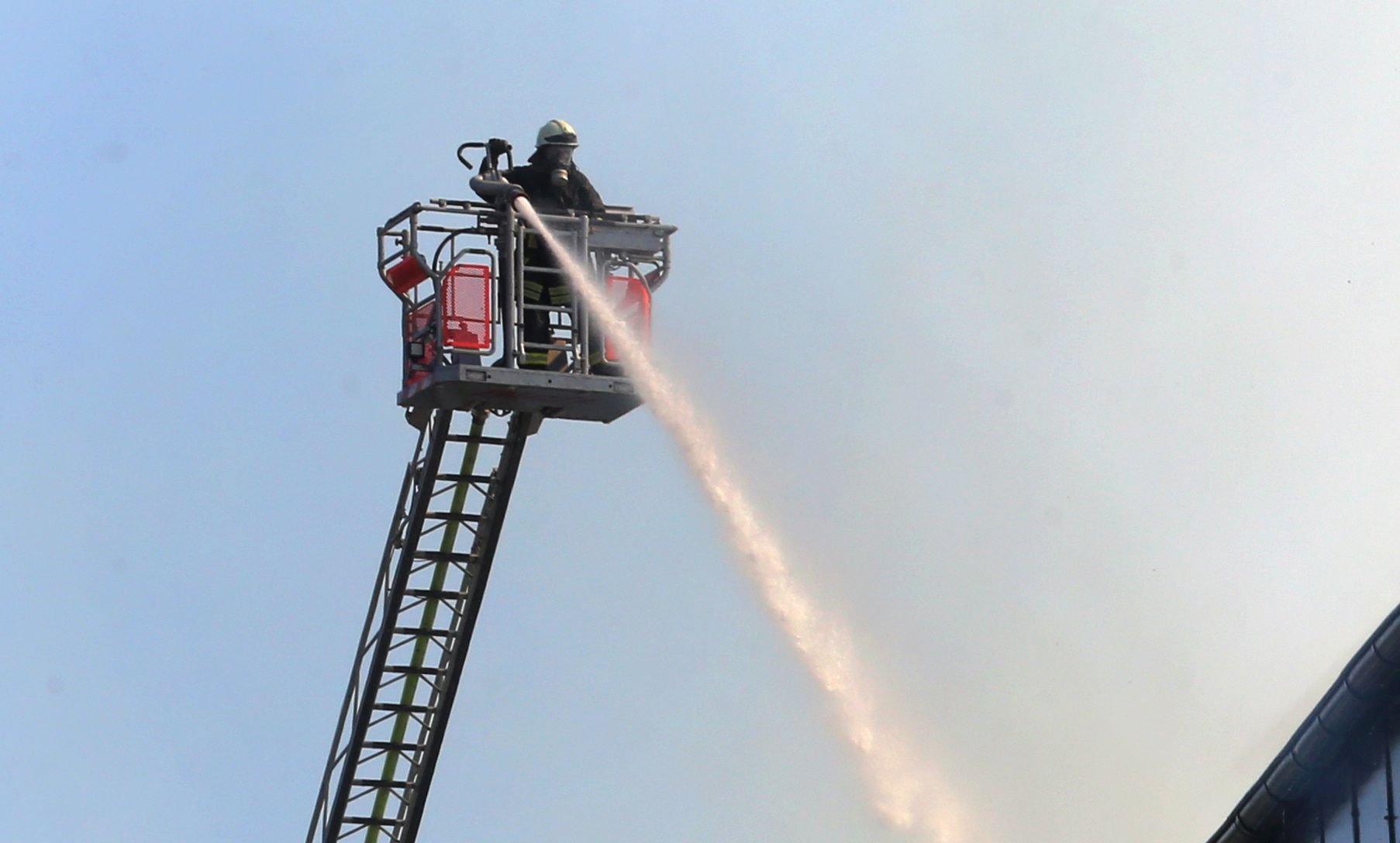 Ein Kamerad der Feuerwehr löscht von einer Drehleiter aus.