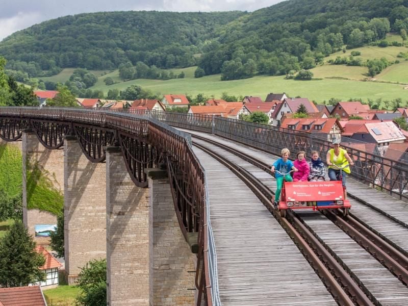 Besucher fahren auf einer Fahrraddraisine. Foto: Michael Reichel/Archiv