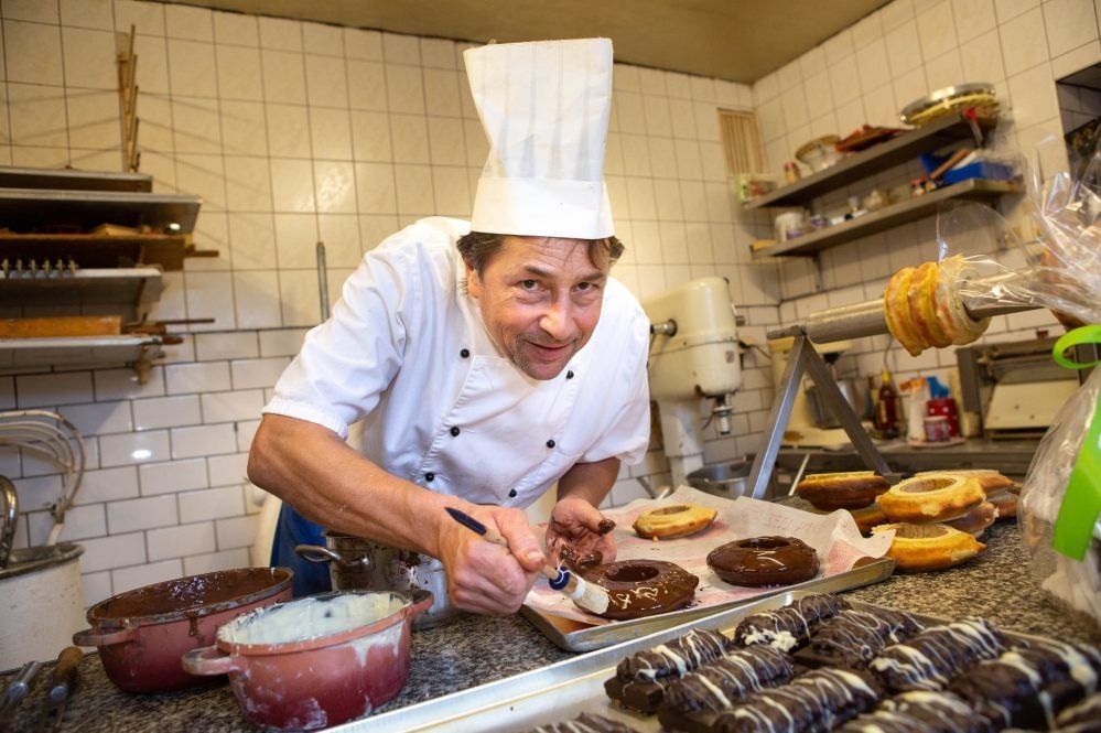 Nachdem er den Baumkuchen in Ringe geschnitten hat, taucht Konditormeister Hardy Kunze das Gebäck in dunkle Schokolade und bessert bei Bedarf mit einem Pinsel nach. Das Naschwerk aus dünnen Teigschichten gibt es bei ihm nur in der Adventszeit.