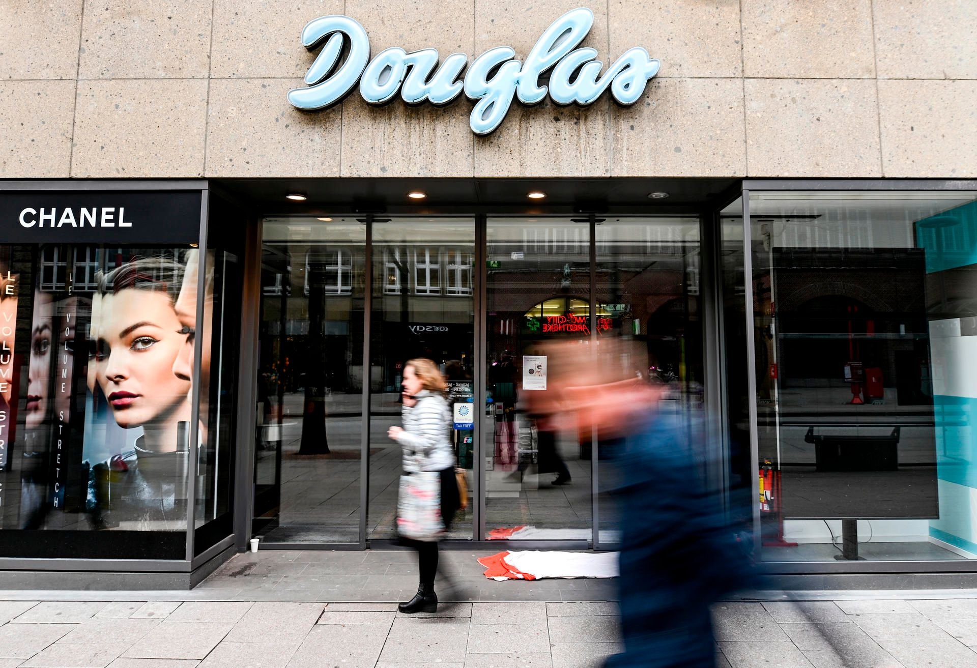 Passanten laufen vor dem geschlossenen Eingang eines Kaufhauses der Parfümerie-Filialkette Douglas in der Innenstadt von Hamburg entlang.