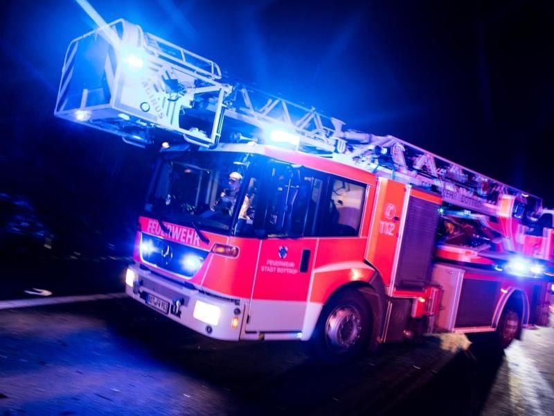 Ein Drehleiterwagen der Feuerwehr fährt mit Blaulicht über eine Straße. Foto: Marcel Kusch/Archiv