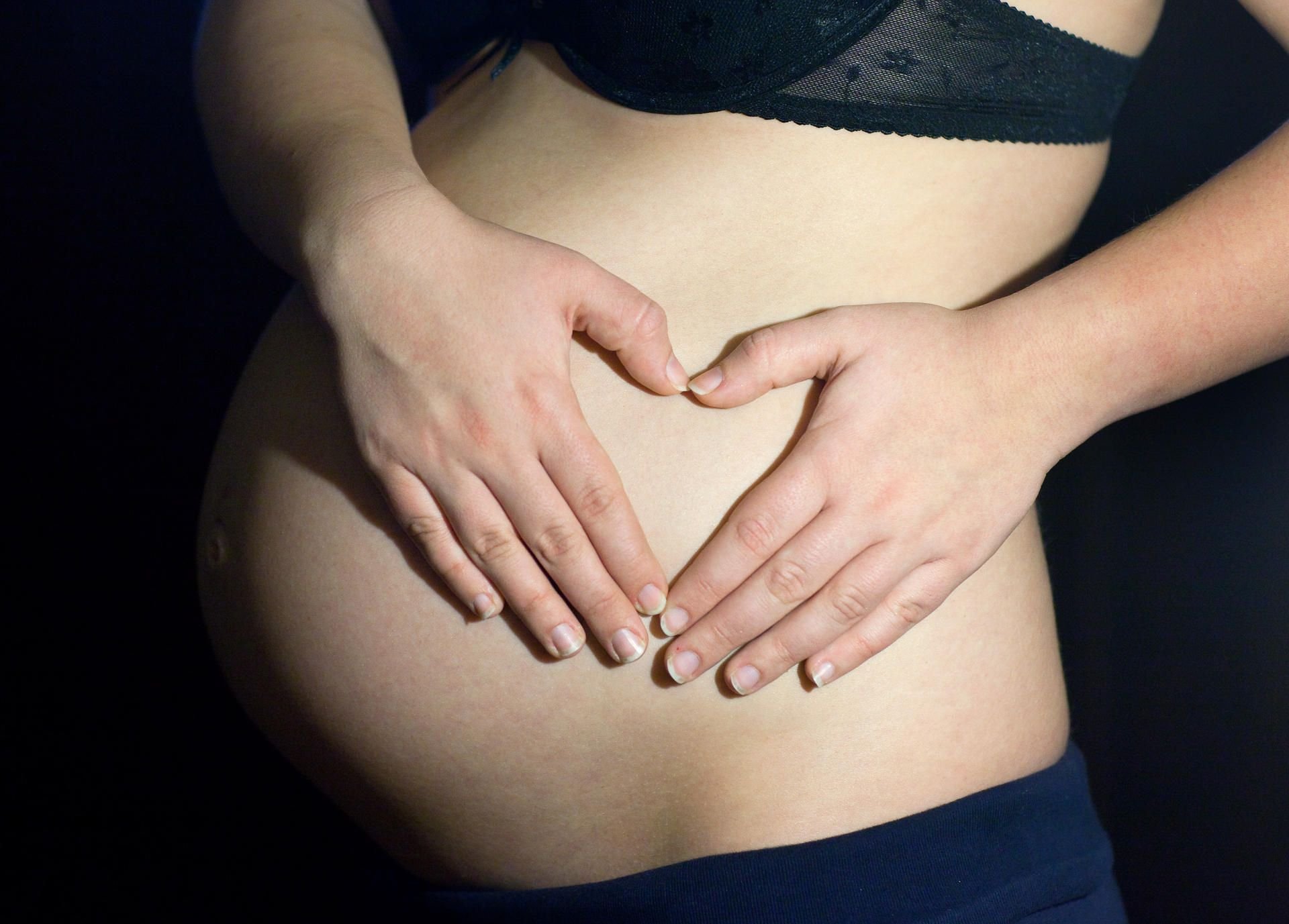 Eine schwangere Frau zeigt ihren Babybauch.