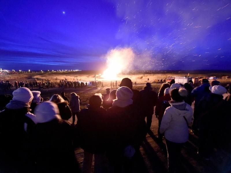 Besucher stehen am Strand vor dem Biikefeuer. Foto: Carsten Rehder/dpa/Archivbild