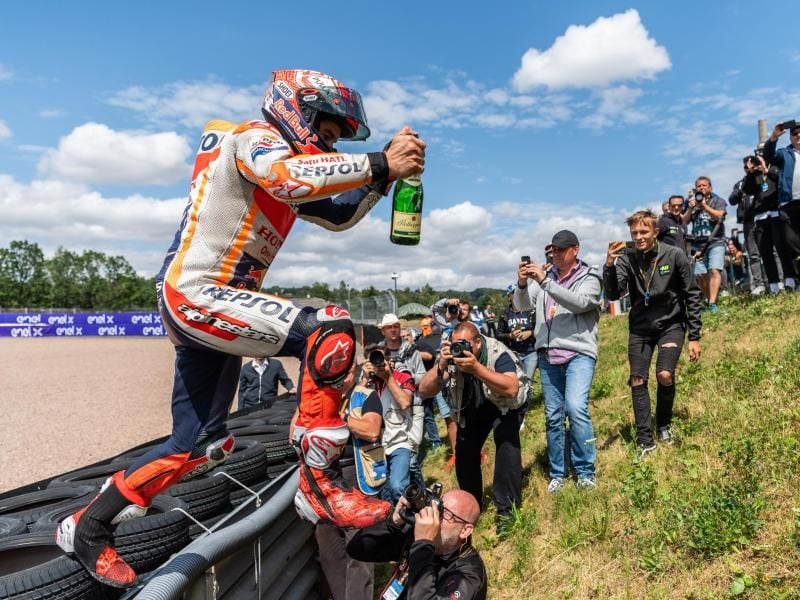 Der Fahrer Marc Marquez (Spanien, Repsol Honda Team) springt nach seinem Sieg mit einer Flasche Sekt in der Hand über die Bande. Foto: Robert Michael