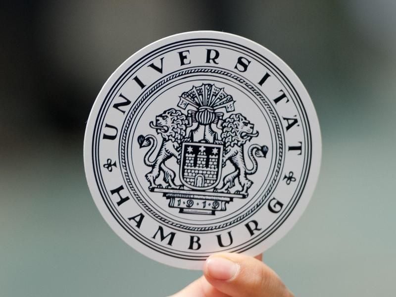 Eine Studentin zeigt nach der Immatrikulationsfeier an der Universität Hamburg einen Aufkleber mit dem Logo der Uni. Foto: Daniel Bockwoldt/Archiv
