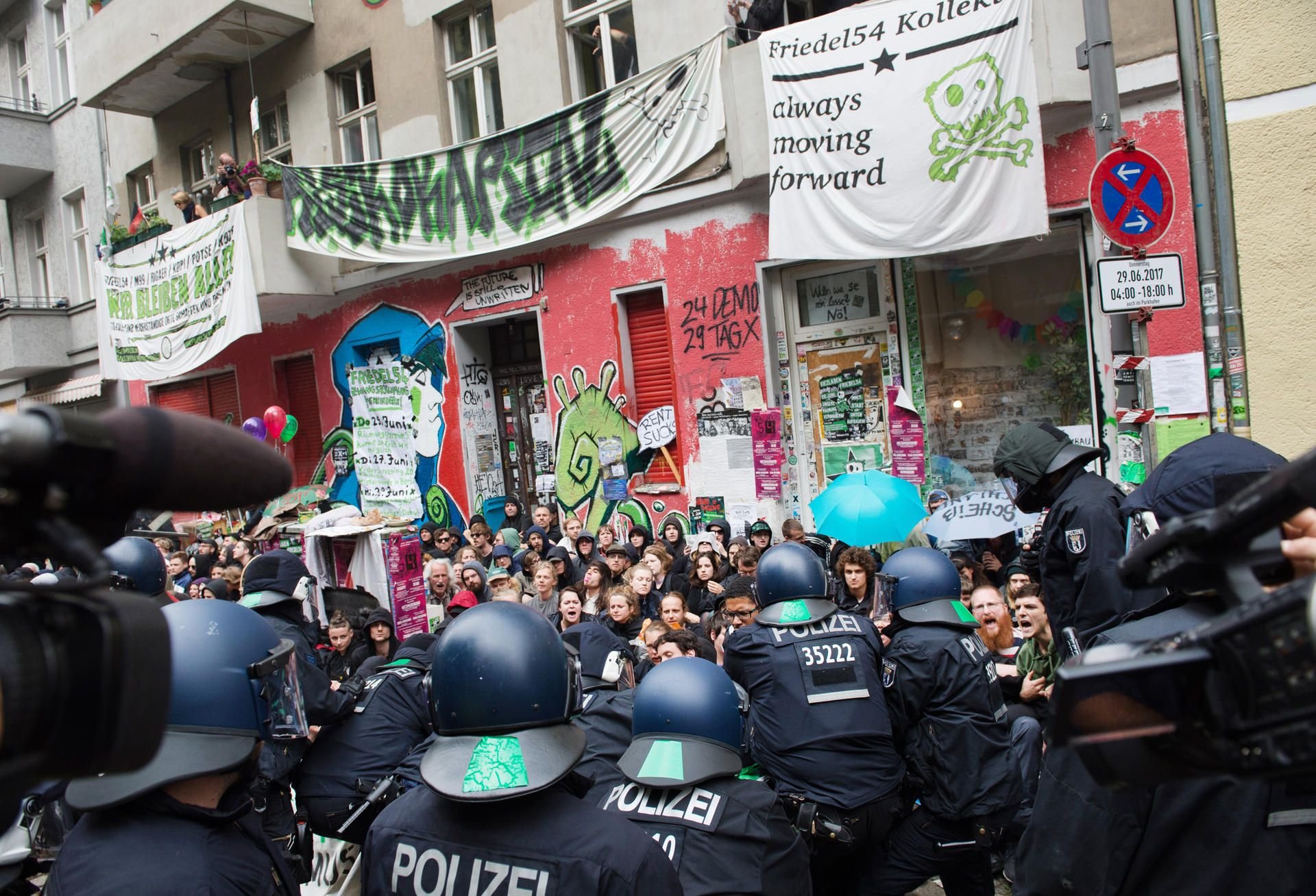Polizisten stehen in Berlin vor dem Haus Nr. 54 in der Friedelstraße in Neukölln, vor dem Demonstranten sitzen.