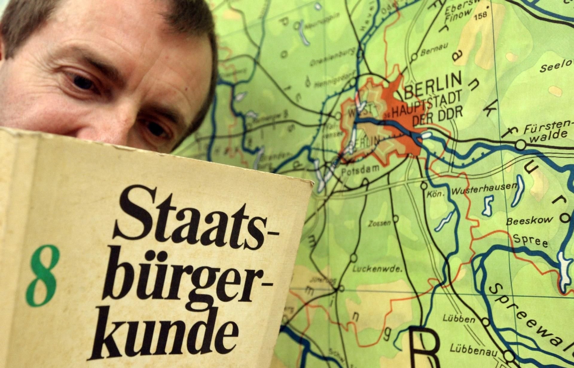 In ein DDR-Schulbuch für die 8. Klasse im Fach "Staatsbürgerkunde" schaut ein Mitarbeiter des Museums Barockschloß Delitzsch vor einer Landkarte.