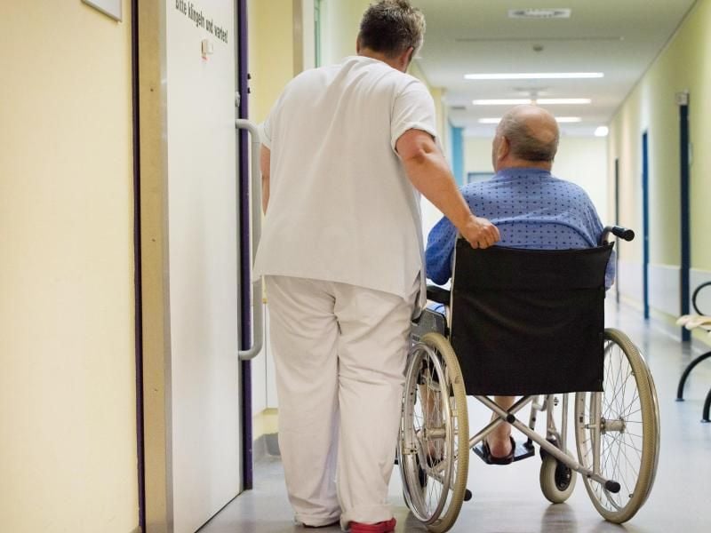 Eine Krankenschwester steht neben einem Patienten im Rollstuhl.