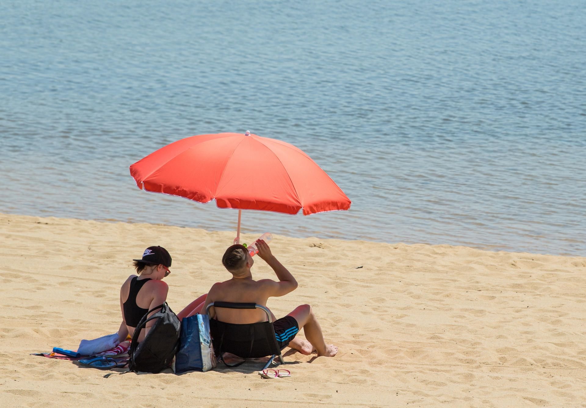 Badegäste sitzen an einem Strand. In den kommenden Tagen werden in Sachsen-Anhalt Temperaturen bis zu 30 Grad erwartet.