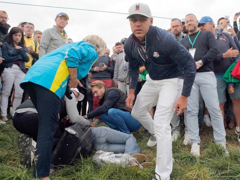 Brooks Koepka (M) vom Team USA steht neben der Zuschauerin, die von seinem Golfball getroffen wurde. Foto: Francois Mori/AP