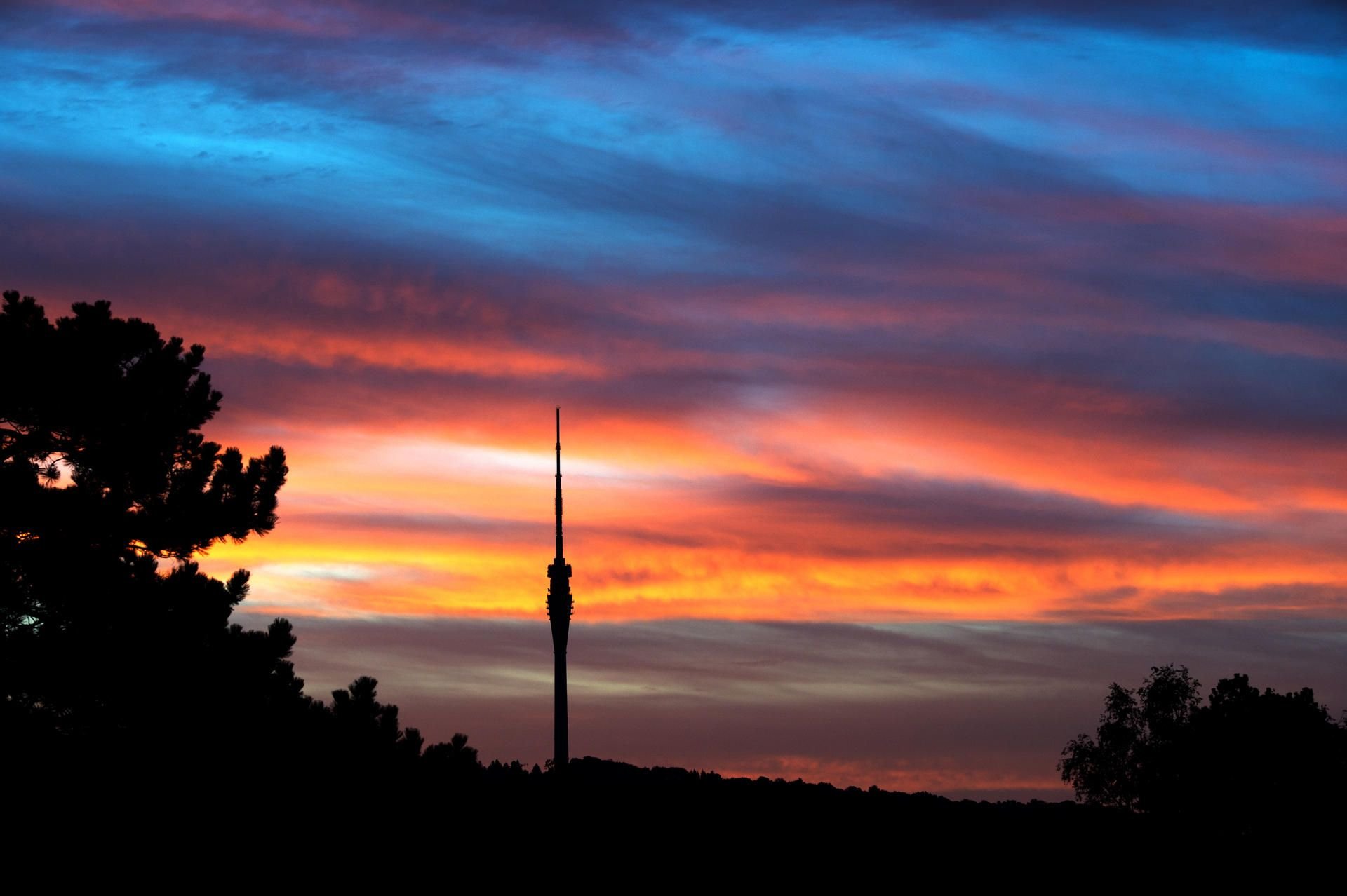 Der Fernsehturm in Dresden zeichnet sich bei Sonnenaufgang vor einem farbigen Himmel ab.