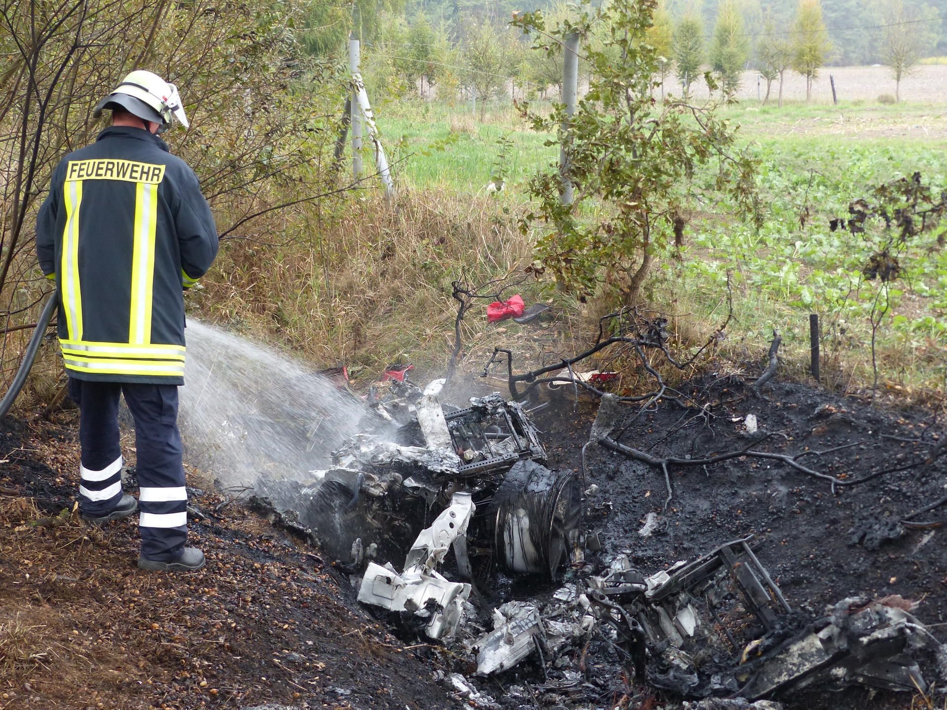in Feuerwehrmann löscht die Überreste des ausgebrannten Ferrari.