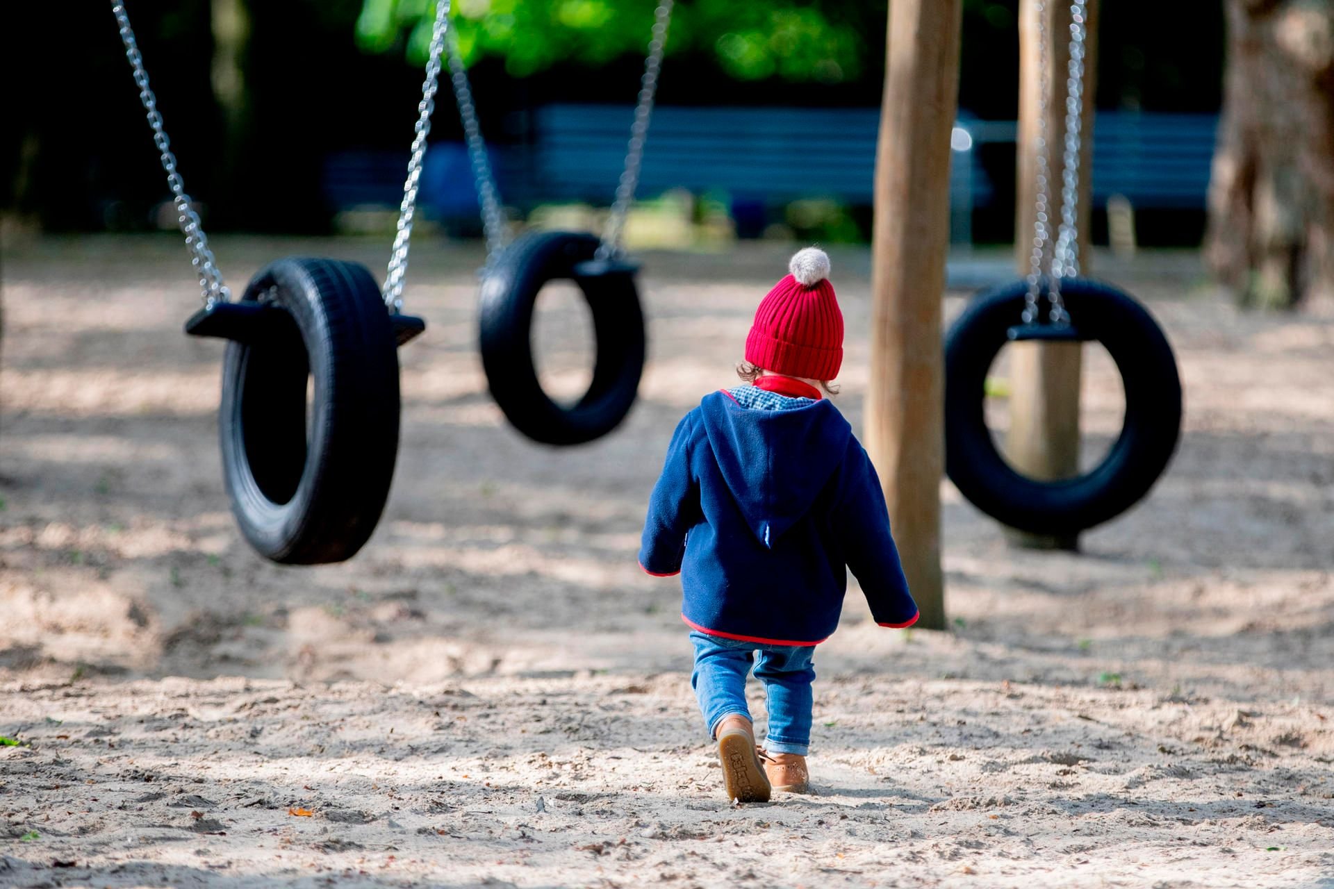 Ein Kind mit Mütze geht geht auf einem Spielplatz zu einer Schaukel. Wochenlang waren Spielplätze in den Städten gesperrt.
