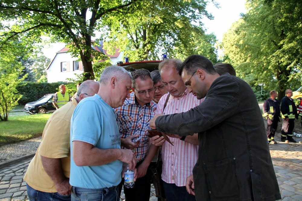 Stadträte sehen sich Handyfotos an, die jemand von der anderen Seite des Sees von der Abbruchstelle gemacht hat.