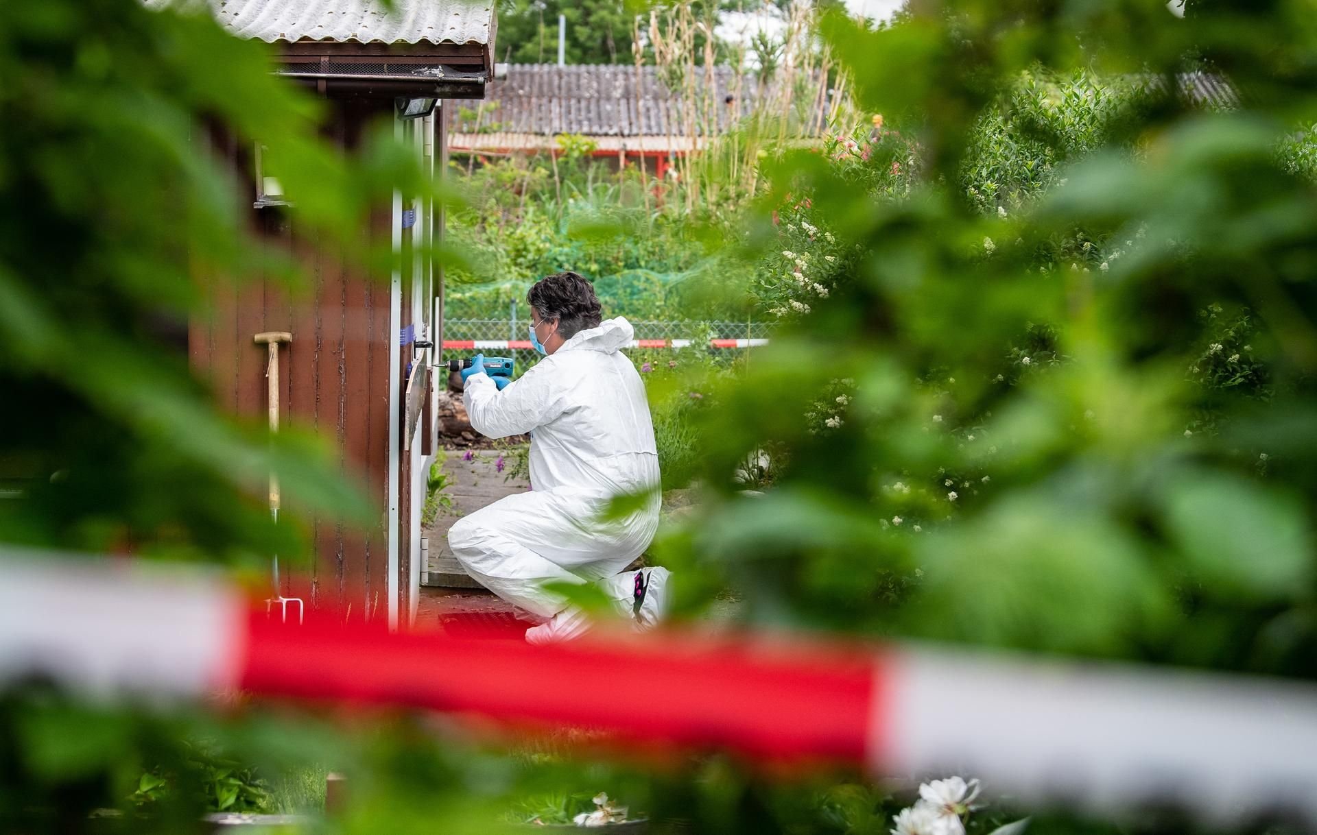 Ein Polizeibeamter der Spurensicherung hockt in der Kleingartenkolonie vor der Laube des vermutlichen Haupttäters.