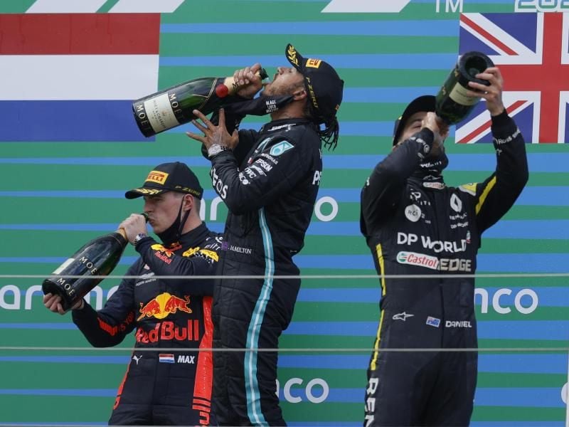 Auf dem Podest genehmigen sich der Zweitplatzierte Max Verstappen (l-r), Sieger Lewis Hamilton und Daniel Ricciardo zunächst einen großen Schluck. Foto: Ronald Wittek/Pool EPA/AP/dpa