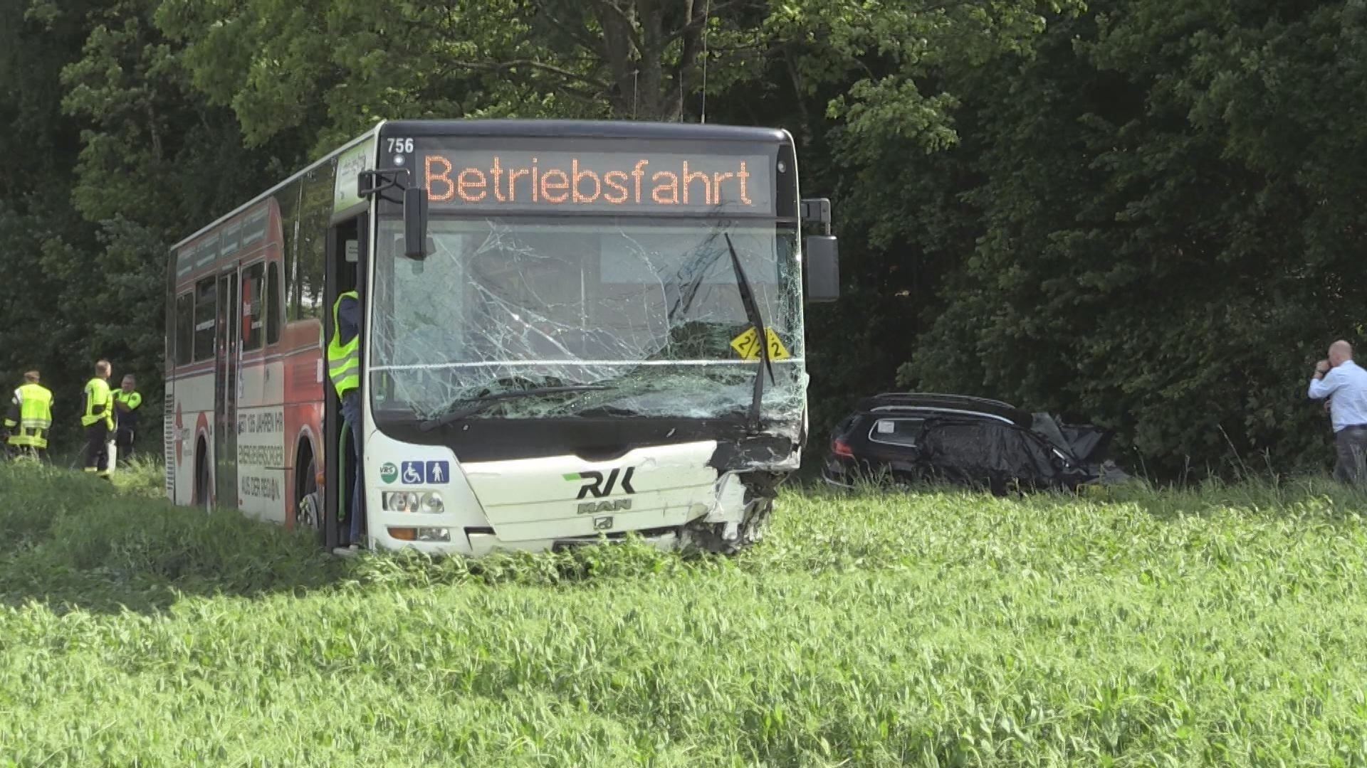 Schwer beschädigt steht der Bus im Feld, im Hintergrund ist der Passat zu sehen, in dem zwei Menschen starben.