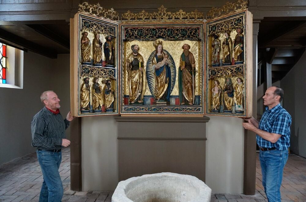 Pfarrer Ronald Höpner und Gemeindekirchenratsvorsitzender Reinhart Bollmann (re.) präsentieren den restaurierten Flügelaltar an der neuen Wand.