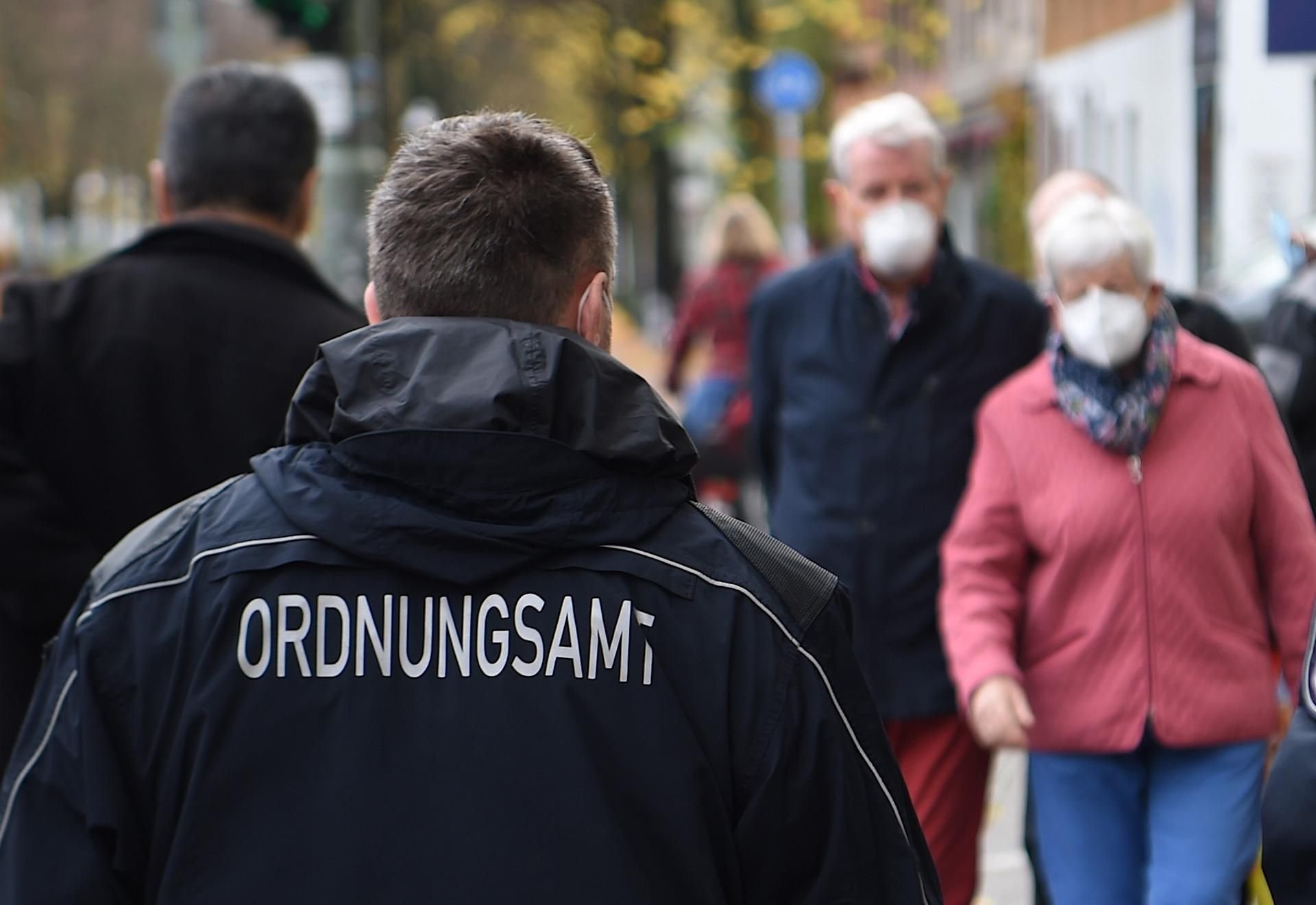 Ein Mitarbeiter eines Ordnungsamtes kontrolliert die Maskenpflicht in einer Innenstadt.