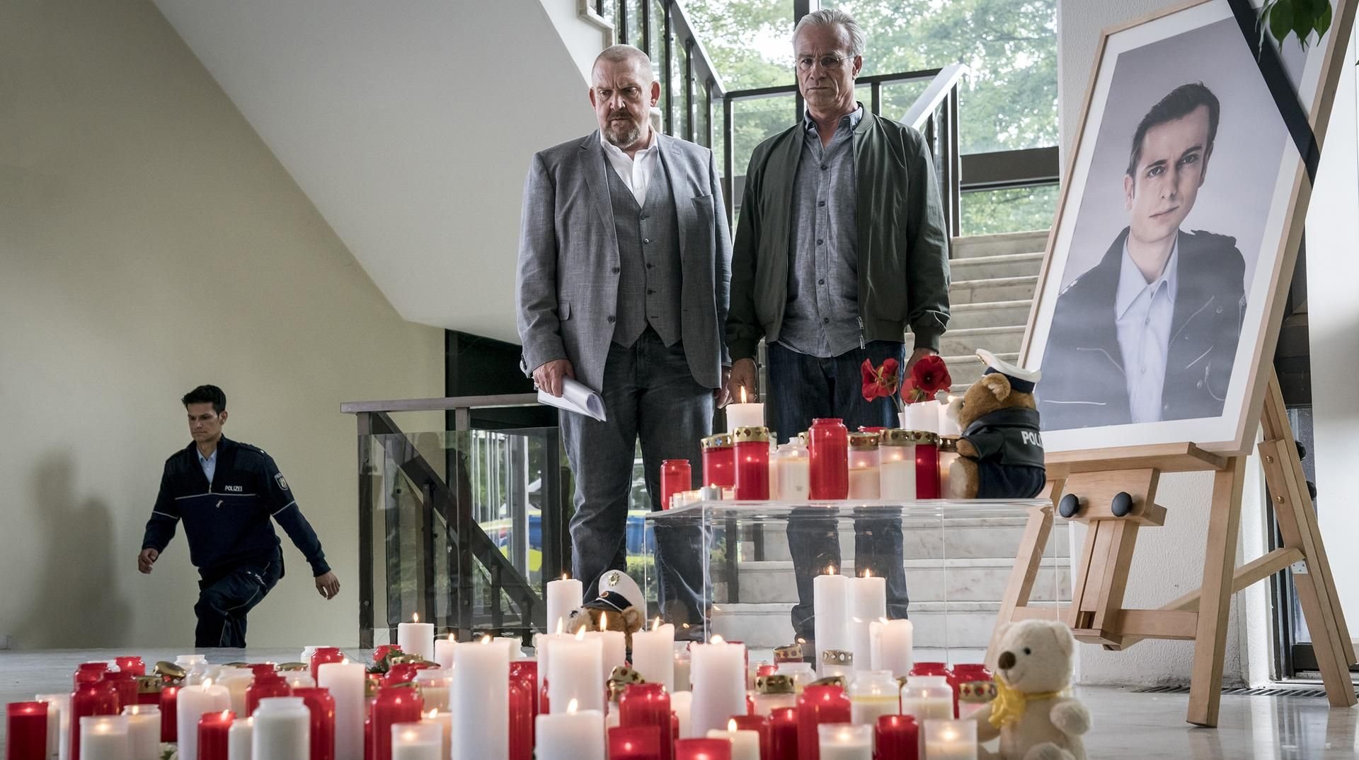 Freddy Schenk (Dietmar Bär, l) und Max Ballauf (Klaus J. Behrendt, r) stehen an dem Ort, wo Kollegen in ihrer Dienststelle an den getöteten Beamten erinnern