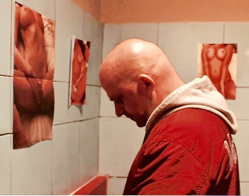 Vandam (Hynek Čermák) auf der Toilette des abgerockten Bierlokals, das stilgerecht mit Männerträumen tapeziert worden ist.