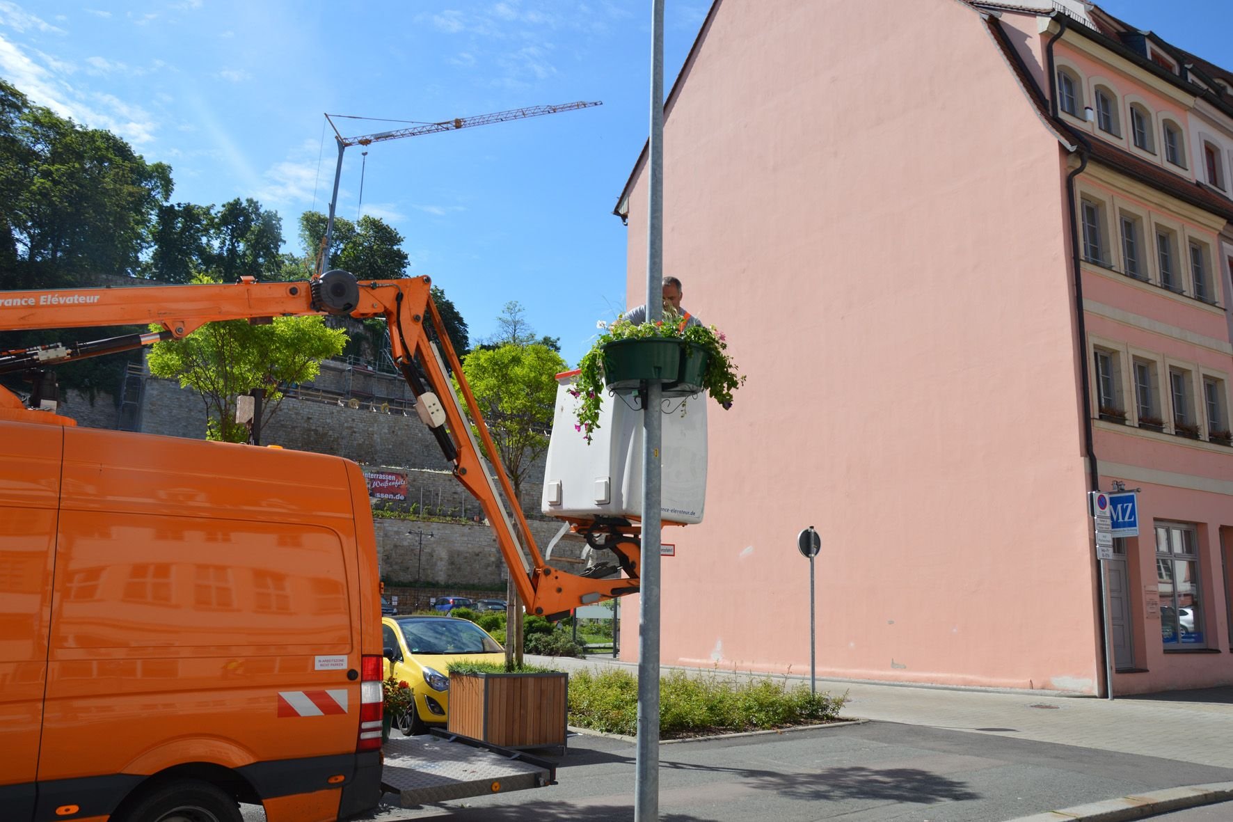 Es blüht in der Weißenfelser Innenstadt: Ein Mitarbeiter der Stadtwirtschaft hängt eine Blumenampel vor dem Fürstenhaus auf.
