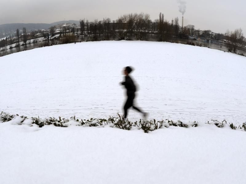 Eine Joggerin läuft an der mit Schnee bedeckten Neckarpromenade in Heidelberg entlang. Foto: dpa