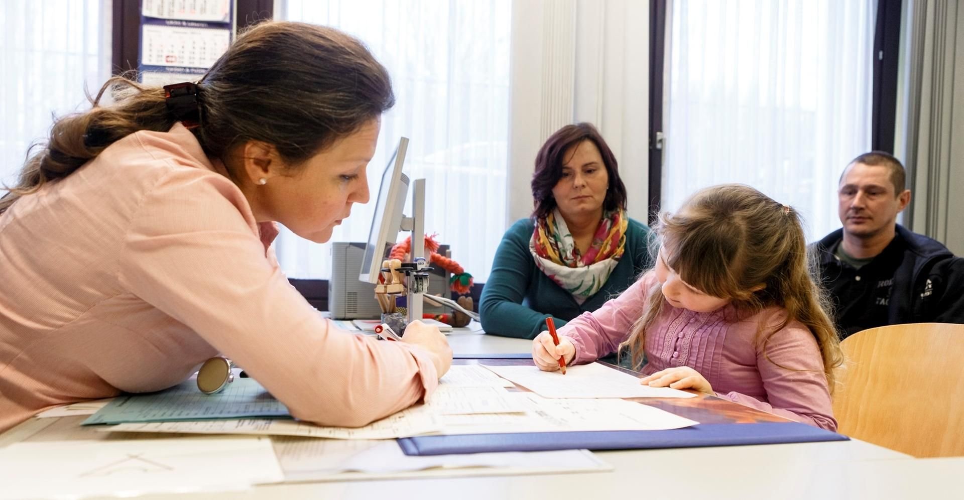 Eine Ärztin führt mit einem fünfjährigen Mädchen im Beisein deren Eltern die Schuleingangsuntersuchung durch.