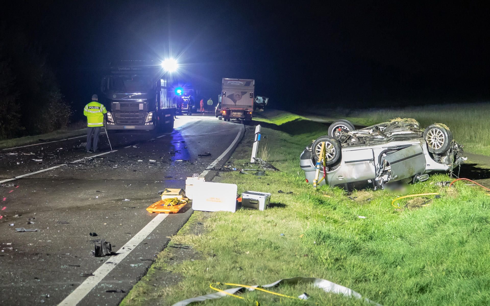 Polizisten vermessen nach einem Verkehrsunfall am Autobahnzubringer S255 bei Hartenstein (Landkreis Zwickau) die Unfallstelle, während Lastwagen auf der Fahrbahn stehen, und ein Auto auf dem Dach neben der Fahrbahn liegt.