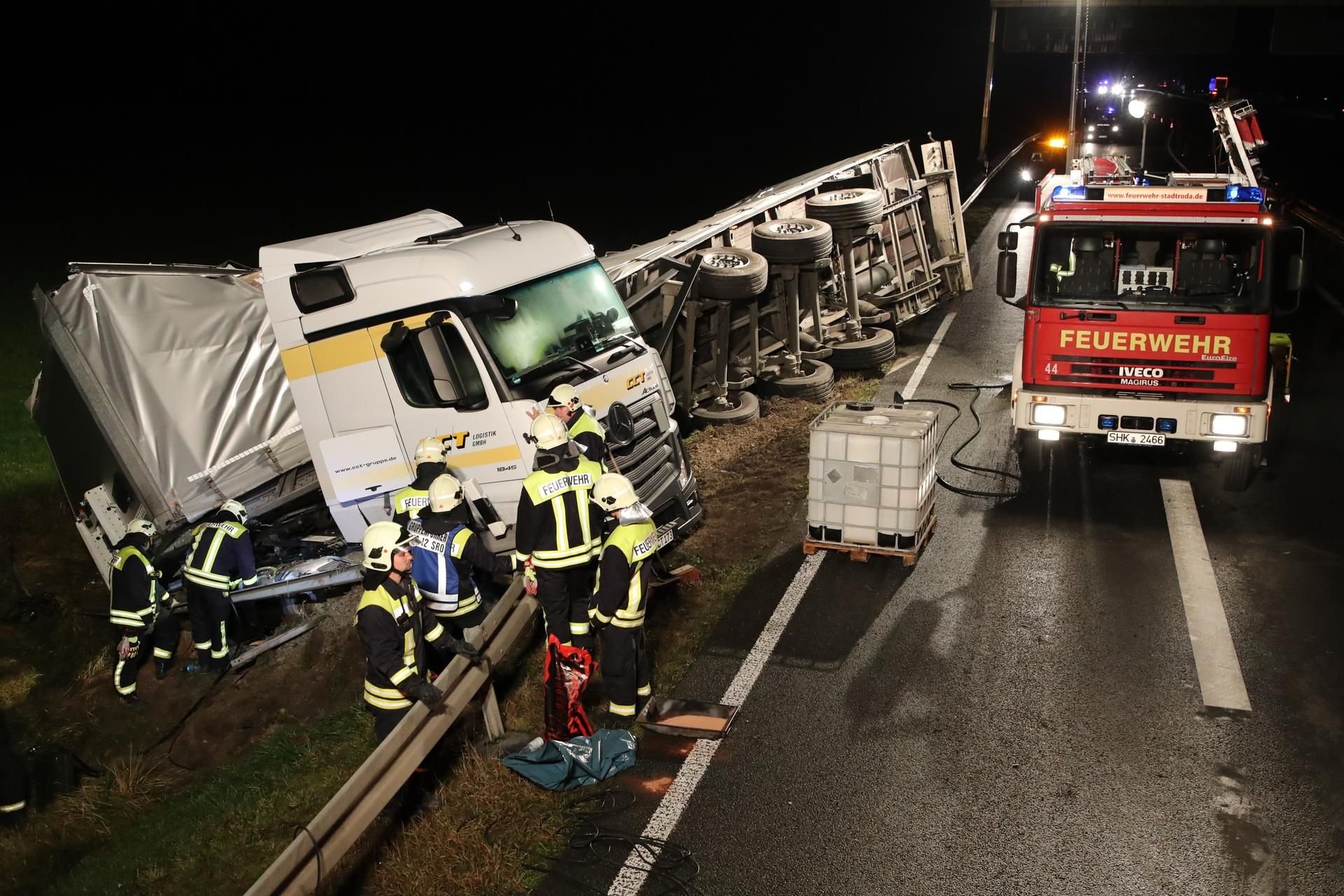 Feuerwehrleute stehen an einem umgekippten Lkw auf der Autobahn 4 am Hermsdorfer Kreuz. Der mit Möbeln beladene Laster war in der Nacht aus noch ungeklärter Ursache von der Fahrbahn abgekommen und umgekippt.