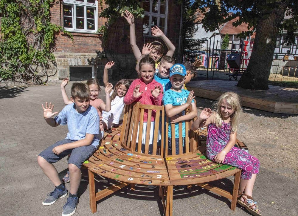 Kinder der Neustädter Grundschule winken von der Sitzbank, die für den Quedlinburger Ökogarten bemalt wurde.