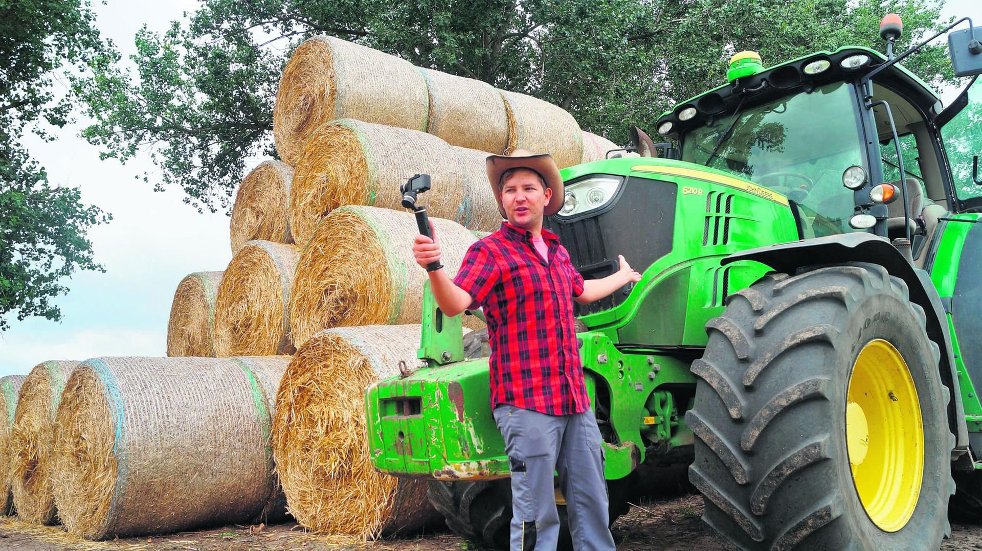Michel Allmrodt steht vor einem Traktor des Landwirtschaftsbetriebs in Schönwalde in der Altmark und spricht in die Kamera.