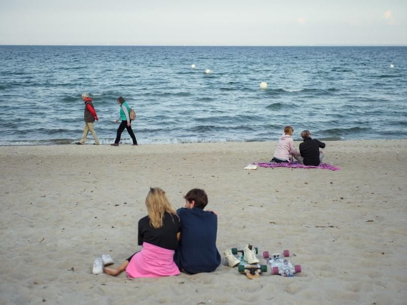 Paare sitzen am Strand der Gemeinde Scharbeutz im Kreis Ostholstein. Foto: Gregor Fischer/dpa/Archivbild
