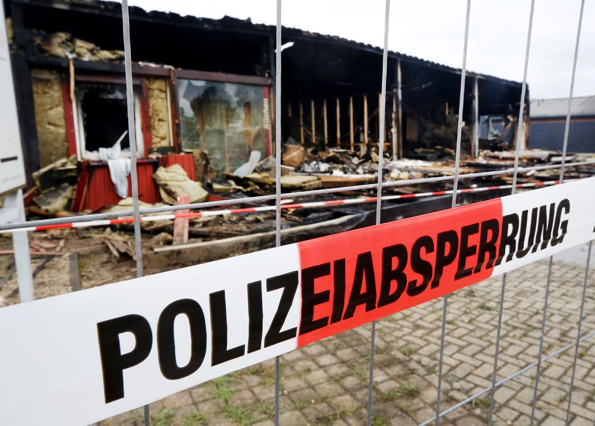 Ein Polizeiabsperrband hängt am Zaun vor den Resten des abgebrannten Saunaclubs in Hamminkeln.