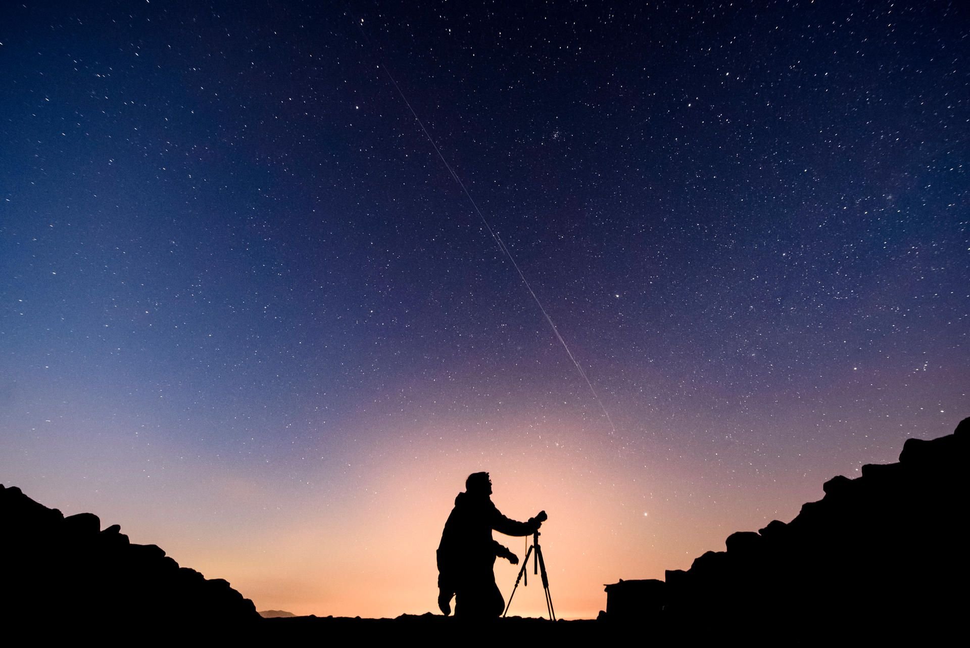 Ein Mann mit einem Fotostativ steht vor einem Nachthimmel. (Symbolfoto)