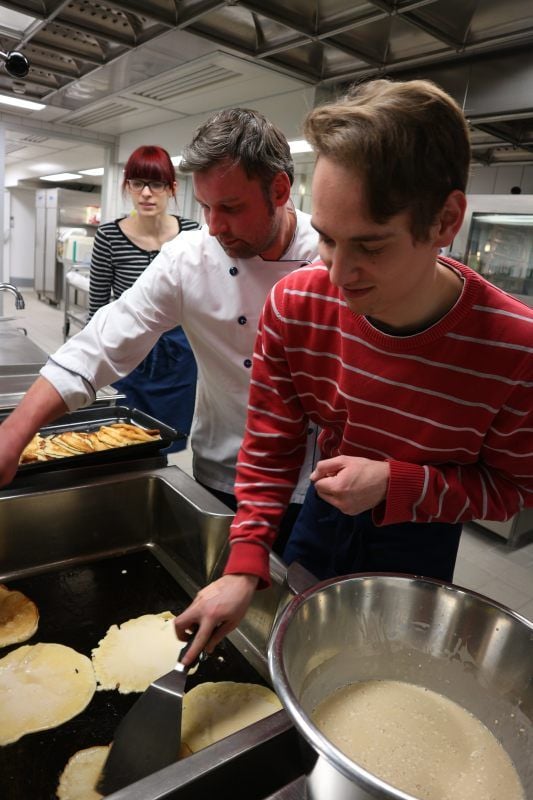 Eric Küchmeister (Mitte) zeigt den Studenten im neuen Kochangebot an der Hochschule Merseburg, wie Eierkuchen gemacht werden.