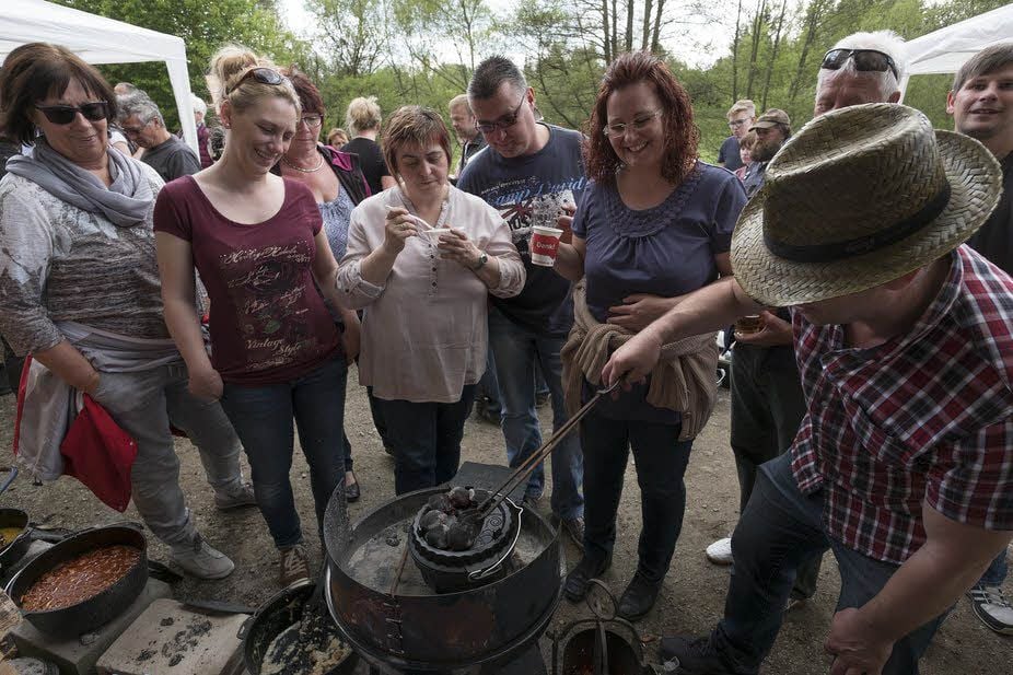 Besucher, aber auch alte Dutch-Oven-Hasen, verfolgen neugierig, wie Kuchenteig in einer gusseisernen Form mit Kohlestücken geheizt wird.