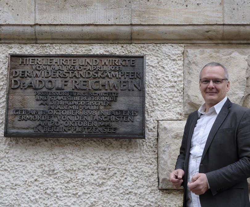 Schulleiter Torsten Gaube steht am Haupteingang des Thomas-Müntzer-Gymnasiums vor der Gedenktafel für Adolf Reichwein.