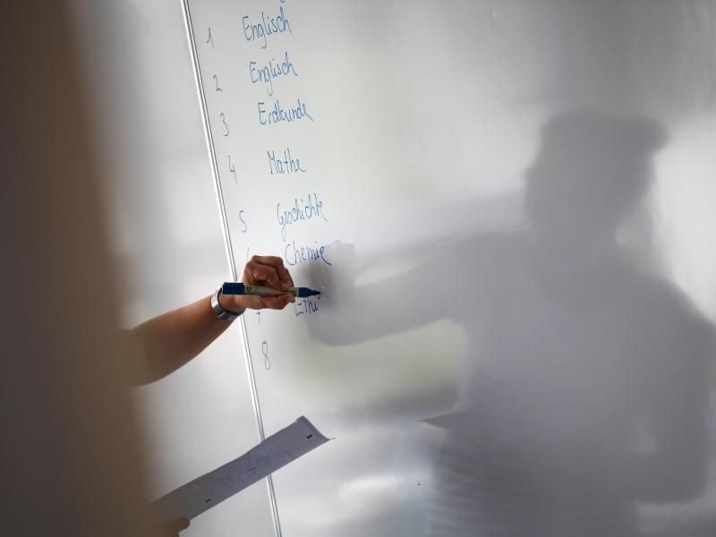 Eine Lehrerin schreibt zu Unterrichtsbeginn den Stundenplan an die Tafel. Foto: Arne Dedert/dpa/Archivbild