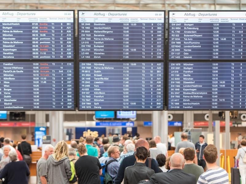 Reisende stehen am Helmut-Schmidt-Airport unter einer Anzeigetafel in einer Schlange. Foto: Daniel Bockwoldt