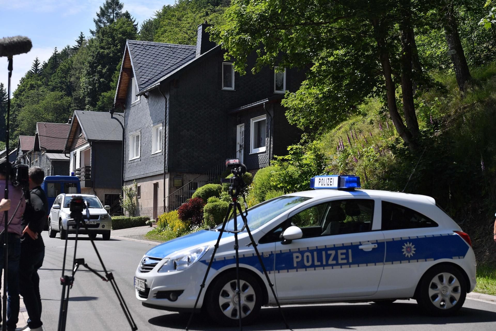 Ein Polizeiauto und Kameras stehen vor dem Haus (vorne rechts) in Altenfeld (Thüringen), in dem sich ein Familiendrama ereignete.