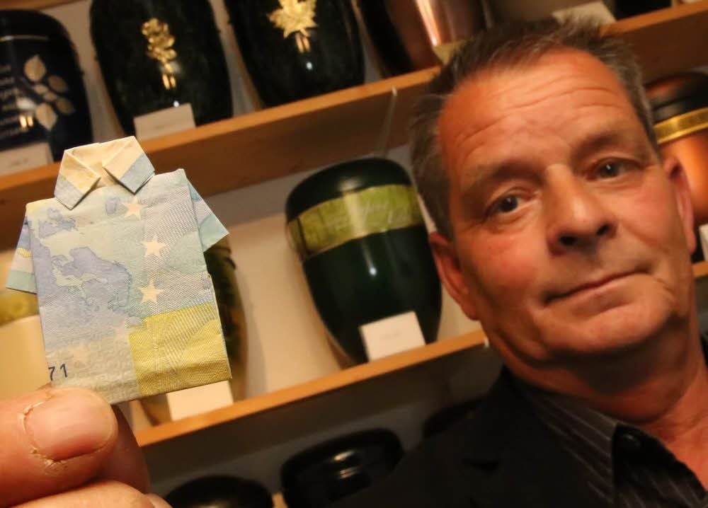 Symbolisch hält Bestatter Gerald Bendlin einen als letztes Hemd gefalteten 20-Euro-Schein in die Kamera.