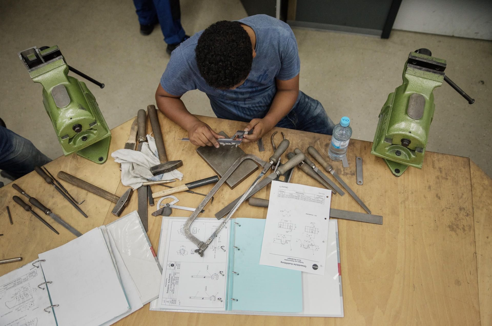 Ein Flüchtling aus Eritrea sitzt an seiner Werkbank und misst ein Werkstück nach.