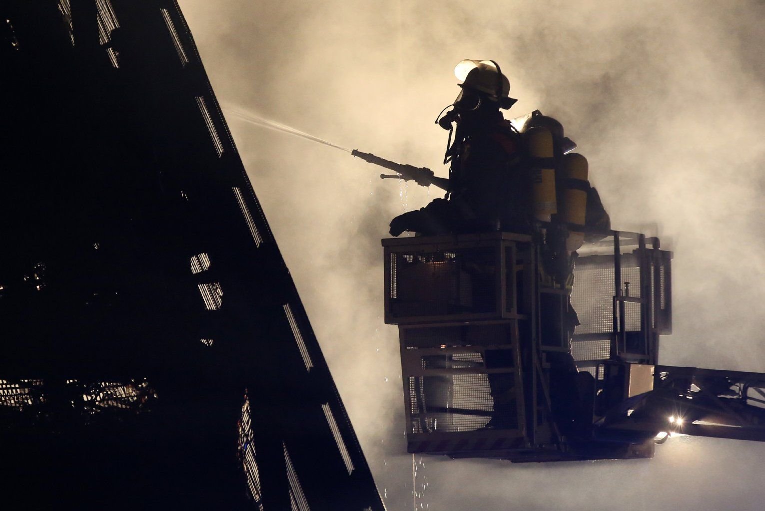 Feuerwehrleute mit Atemschutzgeräten löschen einen Brand von einer Drehleiter aus.