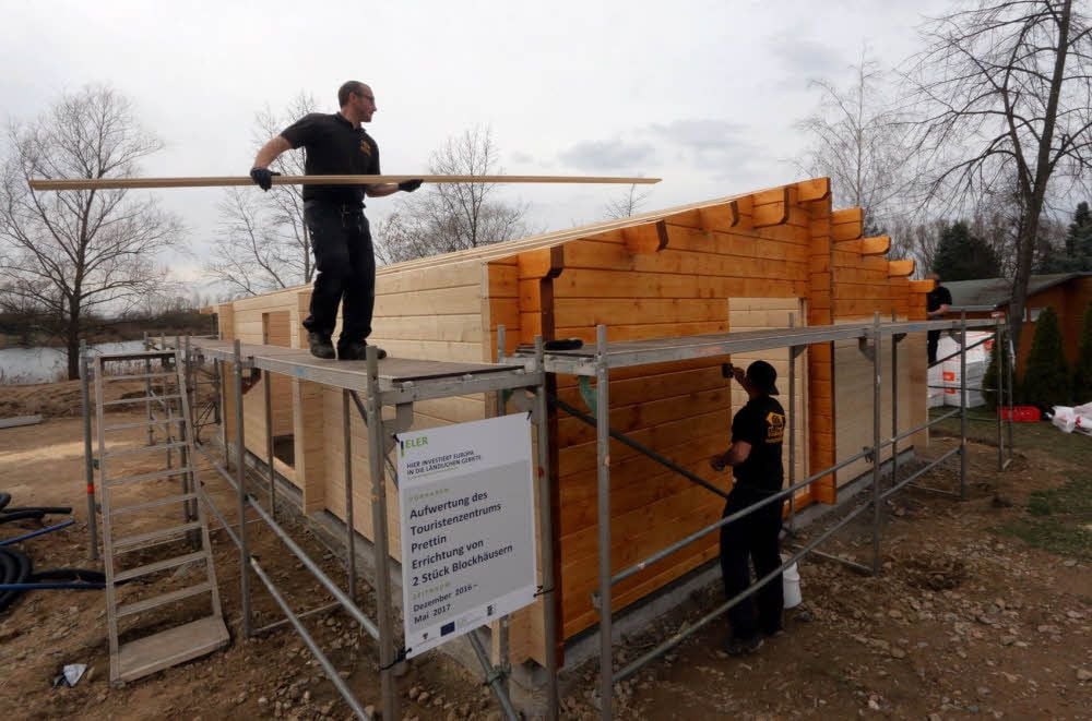 Im Touristenzentrum in Prettin werden derzeit zwei Holzblockhäuser aufgebaut. Darum kümmern sich Fachleute einer Firma aus Großkoschen bei Senftenberg im Nachbarland Brandenburg.