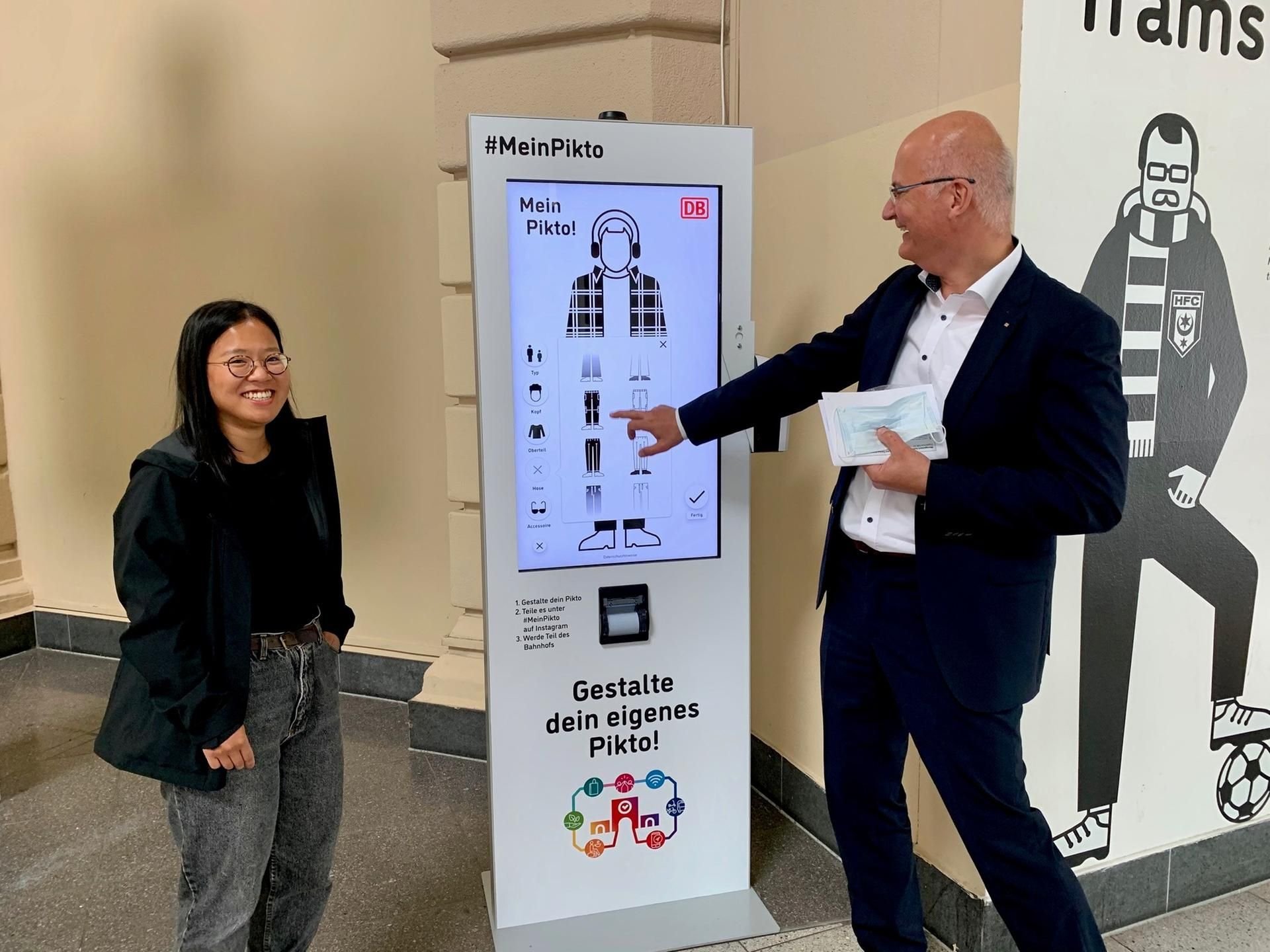 Designerin Han Le und Bahnhofsmanager Karsten Kammler an der Stele, auf der die Piktogramme erstellt werden können.