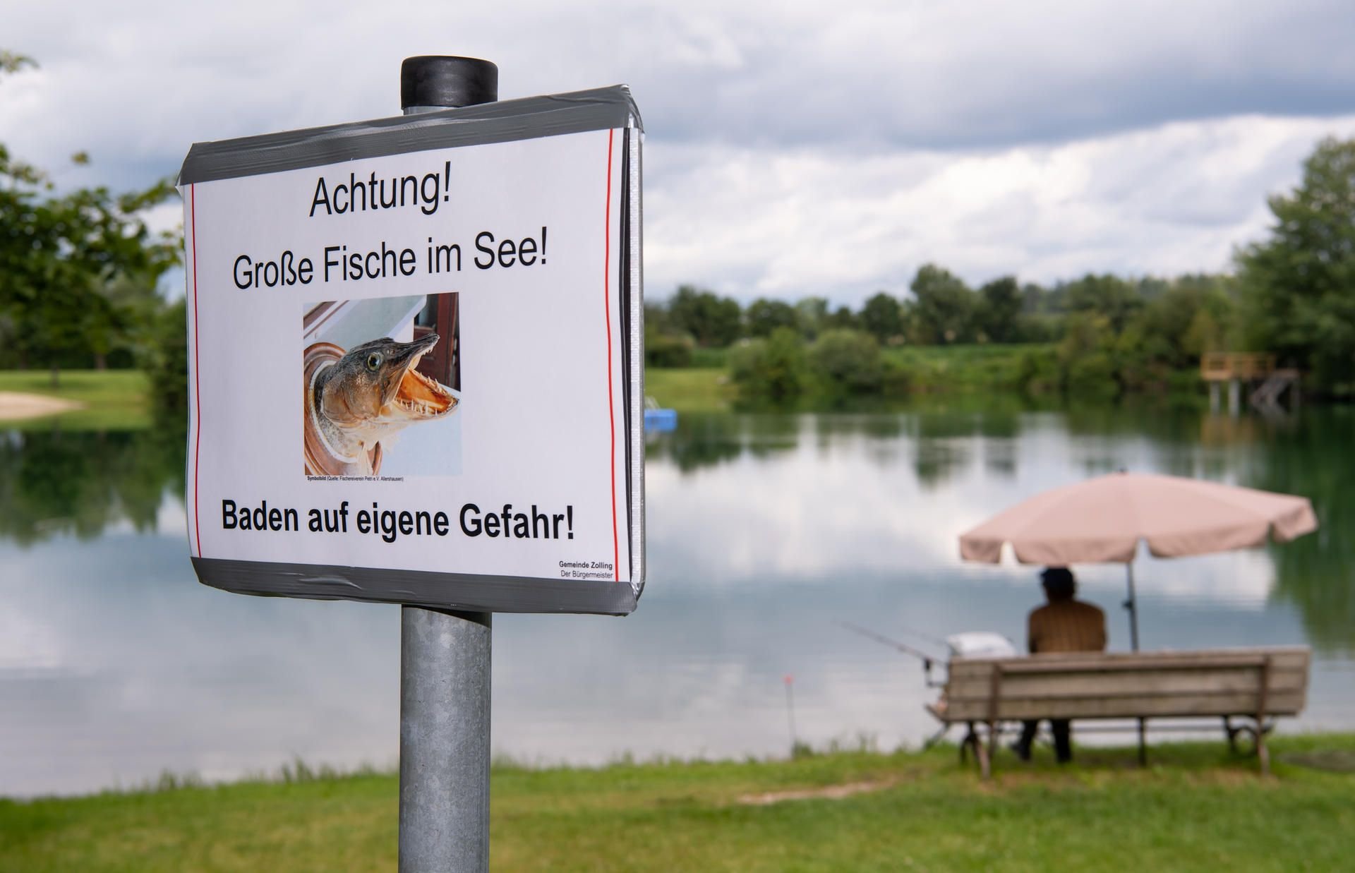 Ein Schild mit der Aufschrift "Achtung! Große Fische im See! - Baden auf eigene Gefahr!" steht am Ufer des Anglberger Weihers in Zolling.