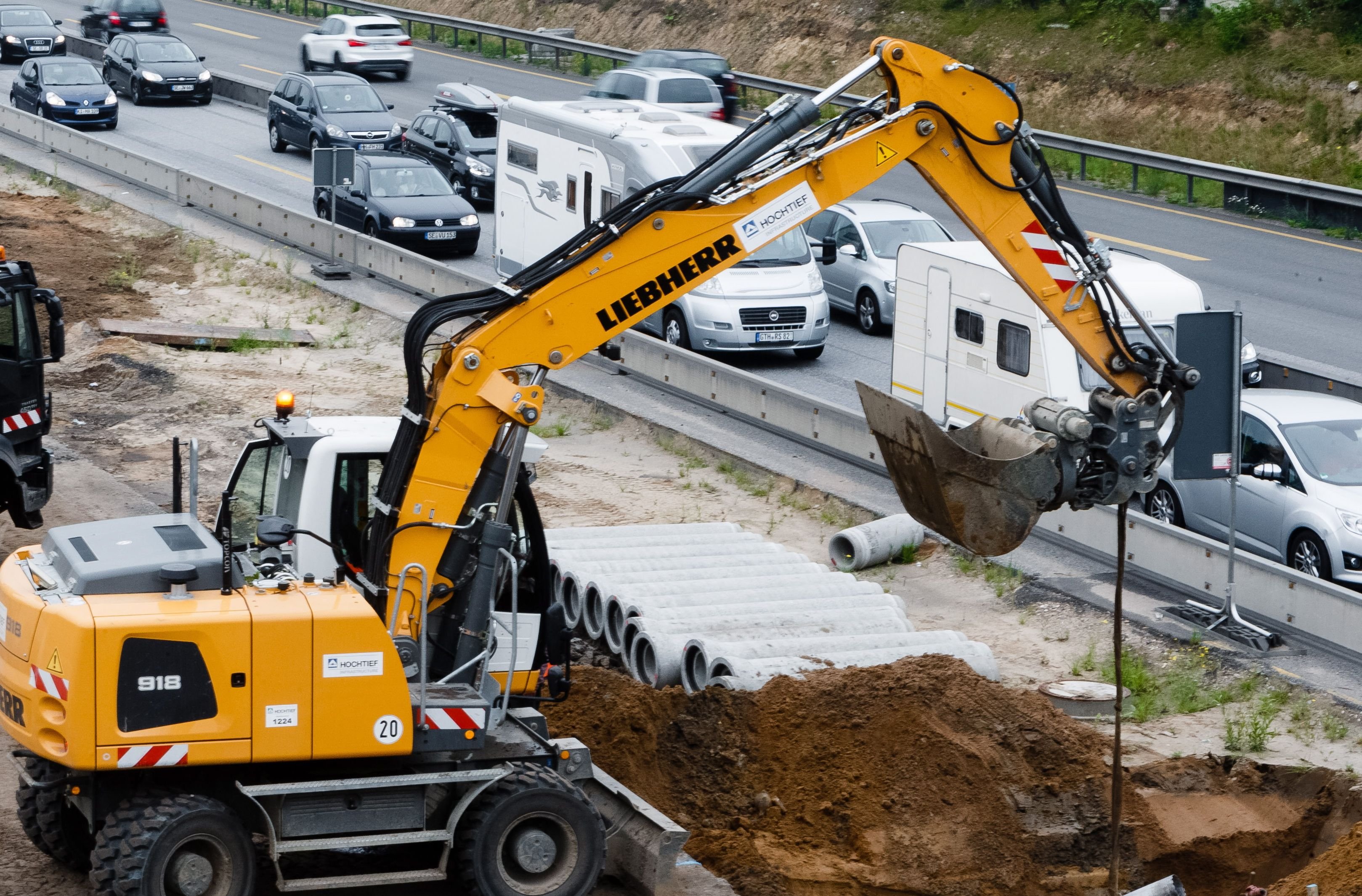 Ein Bagger steht an einer Baustelle an einer Autobahn.